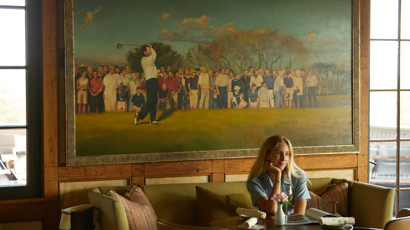 Woman sitting in clubhouse of golf club enjoying herself wearing blue golf dress
